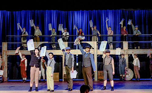 Students on the stage performing a scene from Newsies
