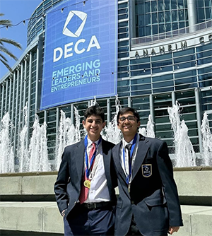 Two male students with medals in front of DECA conference building